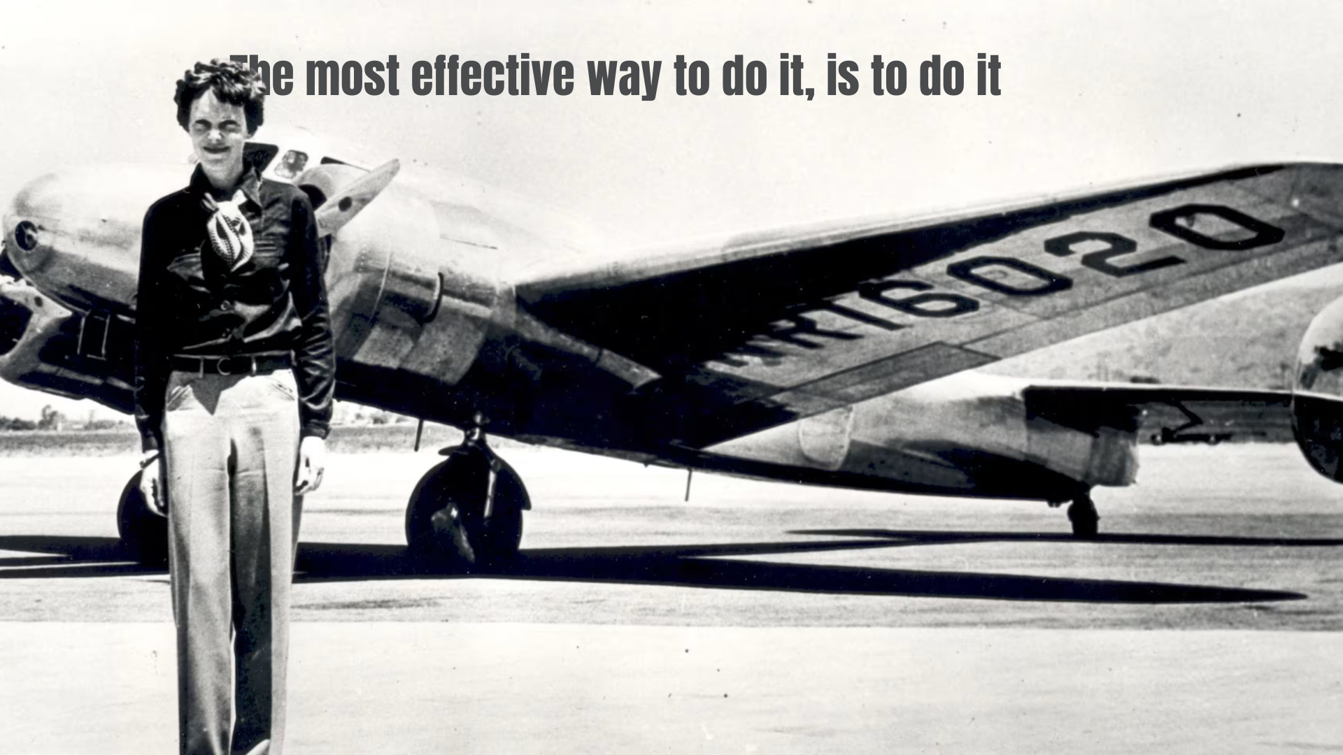 Black-and-white photograph of Amelia Earhart standing in front of her Lockheed Electra airplane.