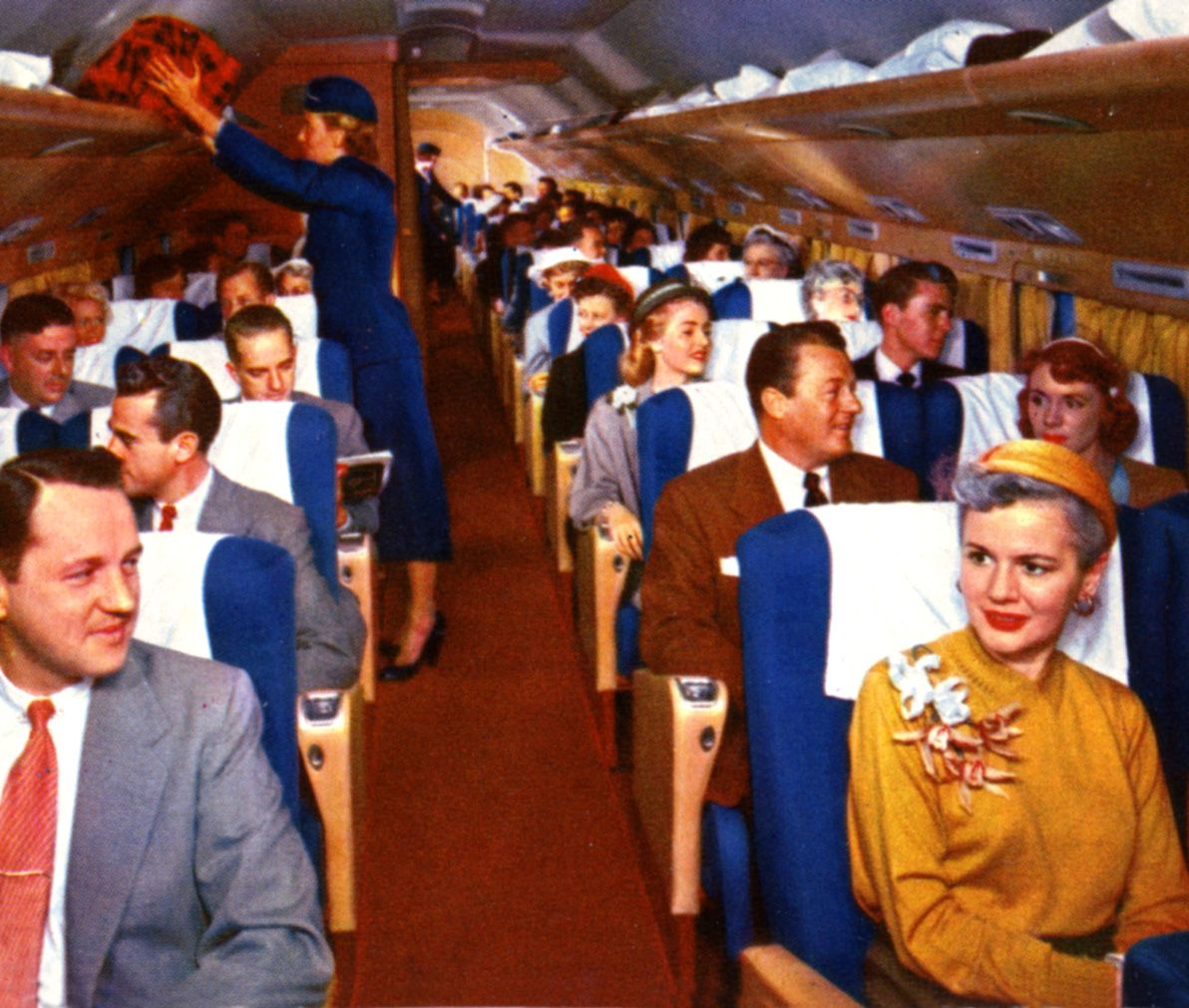 Color photograph from the 1950s showing passengers in formal attire seated inside an airplane cabin.
