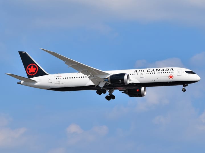 An Air Canada Boeing 787-9 Dreamliner with landing gear extended, approaching for landing against a partly cloudy sky.